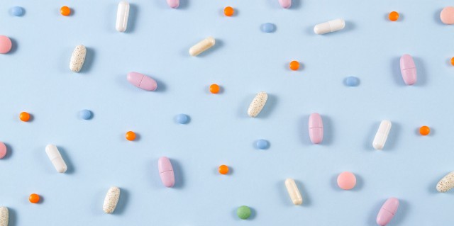 Various colors and sizes of vitamin and supplement pills scattered on a light blue background